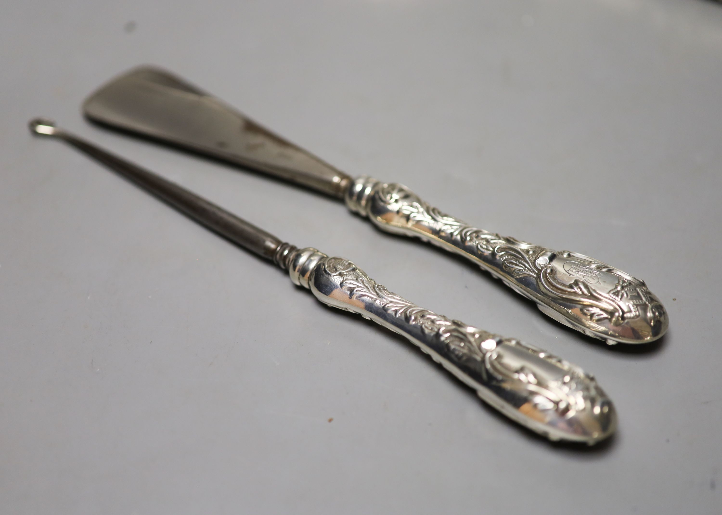 A late Victorian repousse silver mounted hand mirror, London, 1899, two silver mounted glass toilet jars, a silver handled button hook, silver handled shoe horn and a clothes brush.